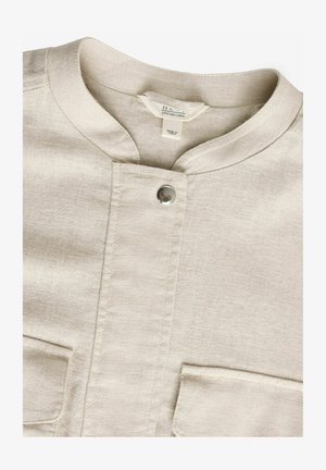 Bela lanena srajca z okroglim ovratnikom, s središnjim zapiranjem na gumb in dvema sprednjima žepoma. Ima subtilno teksturo in minimalističen dizajn.