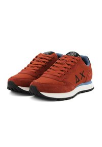 Ein Paar rostorange Sneaker mit schwarzen Symbolen an den Seiten, blauer Innenausstattung, schwarzen Sohlen und weißen Zwischensohlen, nach rechts geneigt.