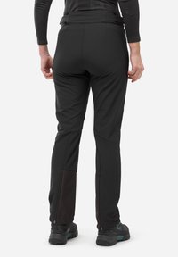 Pantalons d'extérieur noirs avec une coupe ajustée, un tissu texturé, des détails avec fermeture éclair au niveau des chevilles et des sections inférieures renforcées.