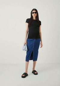 Čierny top s krátkymi rukávmi, modrá džínsová ceruzková sukňa s predným rozparkom, sivá kabelka a čierne sandále. Modelka má na sebe čierne slnečné okuliare.