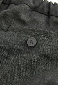 Tissu gris présentant une surface texturée, avec un bouton noir cousu sur la taille. Le tissu est légèrement froissé.