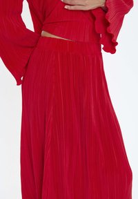 Outfit rosso a pieghe con tessuto testurizzato, maniche lunghe con bordi arricciati e vita elasticizzata per una vestibilità comoda.
