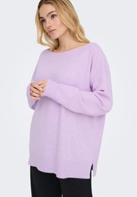 Jasnofioletowy sweter z dzianiny, dekolt w łódkę, ściągacze na mankietach i u dołu, boczne rozcięcia, luźny krój, miękka tekstura. Poniżej widoczne czarne spodnie.