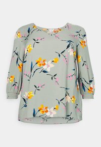 Blusa floreale verde chiaro con maniche a tre quarti, decorata con fiori gialli e rosa su un tessuto morbido, con polsini elasticizzati.