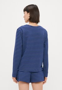 Ναυτικό μπλε μπλούζα μακρύ μανίκι με λευκές ρίγες, συνδυασμένη με ταιριαστά σορτς. Μαλακό ύφασμα με χαλαρή εφαρμογή, διαθέτει στρογγυλή λαιμόκοψη.