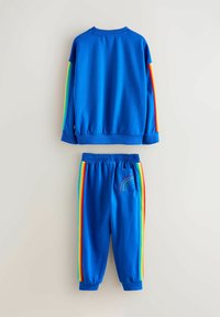 Hanorac albastru cu dungi multicolore pe mâneci, asortat cu pantaloni albaștri cu dungi în culorile curcubeului și un detaliu cu buzunar. Material din bumbac.