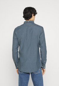 Donkerblauwe overhemd met lange mouwen en een knoopsluiting-kraag, rugplooi en contrasterende knopen. Katoenmix stof met een gestructureerde afwerking.