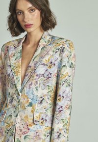 Blazer in lino floreale caratterizzato da una combinazione di colori pastello, revers a punta e tasche frontali, con una texture leggera e una finitura morbida.