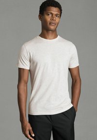 Tricou scurt, de culoare bej deschis, realizat dintr-un material texturat, cu un design ajustat, guler rotund, asortat cu pantaloni închiși la culoare.