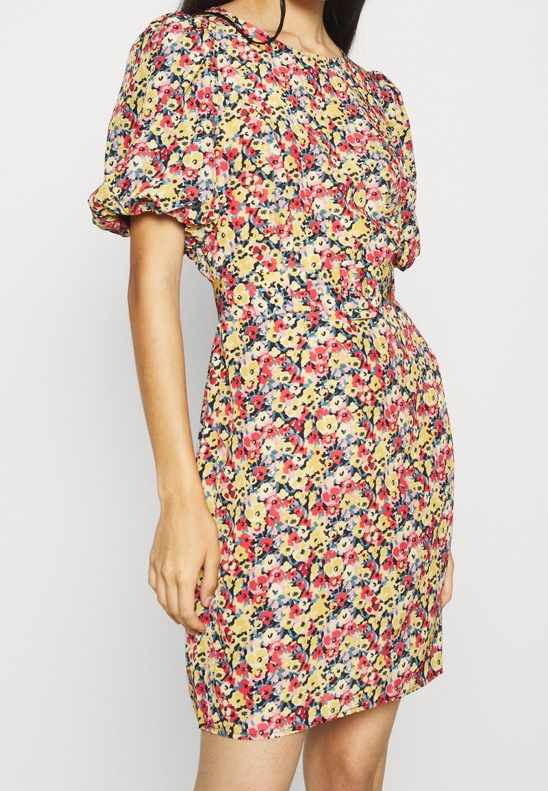 Blumenkleid mit einer Mischung aus rosa, gelben, blauen und grünen Blumen auf gelbem Hintergrund. Kurze Puffärmel, taillierte Silhouette und über knielange Länge.