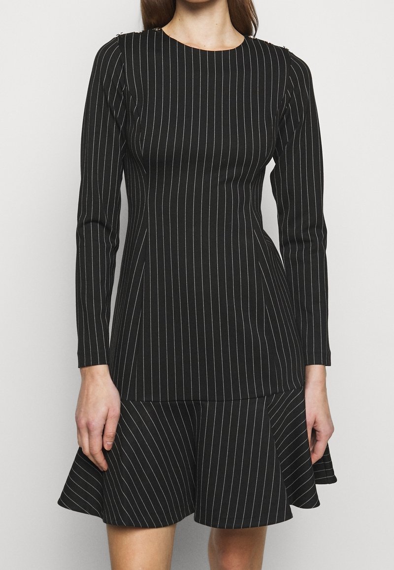 Černé šaty s vertikálními bílými pruhy, dlouhými rukávy, přiléhavým živůtkem a rozšířenou sukní. Materiál se zdá být hladký; má kulatý výstřih.