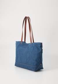 Denim tote bag with brown leather straps, rectangular shape, double stitch accents, and subtle pocket details on the front and side.