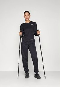 Svart långärmad topp och byxor, båda med subtila logotyper, kombinerade med vandringsstavar och svarta sneakers. Mjukt tyg och atletisk passform.