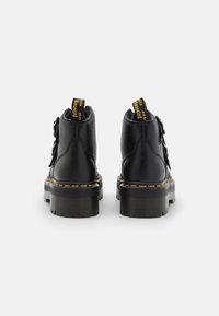 Botines negros de cuero con acabado texturizado, suela gruesa, costuras amarillas y lengüetas prominentes en el talón con logotipo.