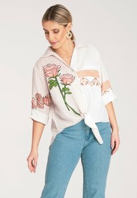 Koszula na guziki w jasnoróżowe i białe paski, z haftem w kształcie różowych róż oraz związanym przodem. Krótkie rękawy i luźny krój.