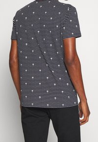 Koszulka w poziome niebieskie paski z małymi białymi motywami palm. Wykonana z miękkiej tkaniny, z krótkimi rękawami i okrągłym dekoltem.