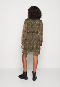 Robe multicolore, transparente, à motifs avec des manches longues et une taille élastique ; portée avec des bottines noires. Detaillée avec une coupe fluide.