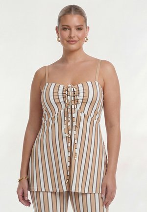 Femme portant un haut sans manches beige et blanc à rayures verticales et un pantalon assorti, souriante, cheveux attachés en arrière et boucles d'oreilles créoles dorées.