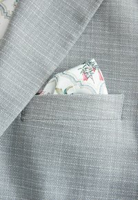 Hellgrauer blazertoff mit Textur, versehen mit einem weißen Taschentuch im Pocket mit einem floralen Muster in Grüntönen, Pink und Blau.