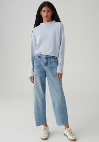 Hellblaues, strukturiertes Langarmoberteil, lockere, hellblaue Jeans mit weitem Bein und weiße Turnschuhe mit beigen Akzenten.