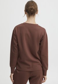 Felpa marrone con maniche lunghe e vestibilità rilassata. Caratterizzata da un collo a giro, tessuto morbido e polsini e orlo a costine.