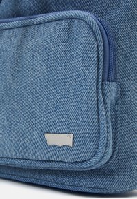 Gros plan d'une poche d'un sac en denim bleu avec une fermeture éclair et un petit logo de marque argenté sur le devant.