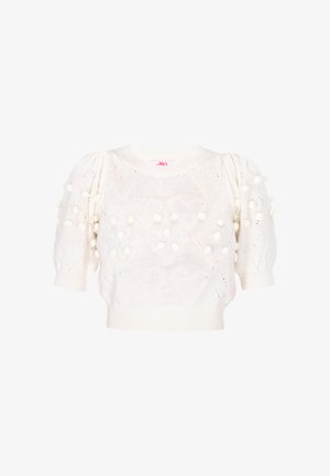 Ung kvinde smilende iført en hvid cropped strik top, lyseblå denimplisseret nederdel med slids foran og orange platform sandaler med ankelstropper.
