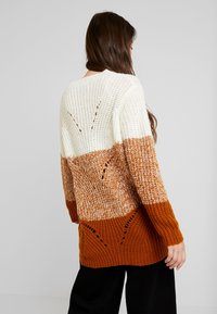 Sweter dzianinowy z kolorowym blokiem w odcieniach kremowym, rdzawym oraz teksturowaną środkową częścią z otwartymi detalami ściegów. Długie rękawy.