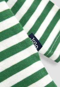 Zaļganais un baltais svītrotais audums ar tekstūru; tam ir tumši zila etiķete ar baltu tekstu. Tuvplāns, kas koncentrējas uz svītrām.