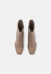 Bottes de cheville en cuir marron avec une finition lisse, un design à bout carré et une fermeture éclair sur le côté pour un enfilage facile.