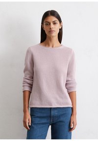 Jasnoróżowy sweter z dzianiny z okrągłym dekoltem, długimi rękawami i prążkowanymi mankietami, w zestawie z niebieskimi dżinsami.
