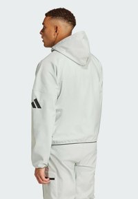 Ljust grå hoodiejacka med avslappnad passform, med svarta accentstrimmor på ärmarna och midjan, samt en slät, matt textur.