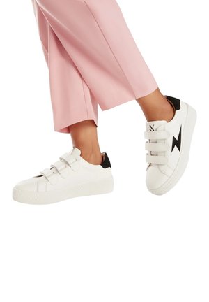 Baskets blanches avec trois bandes velcro, accent noir au talon, semelle en caoutchouc texturée et motif d'éclair sur le côté.