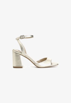 Sandală cu toc pătrat, cu vârf deschis, curea la gleznă și finisaj metalic aurit. Textură netedă și detalii minime.