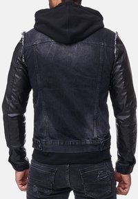 Zwarte denimjack met leren mouwen, rafelige kraagdetail en geribbelde zoom. Beschikt over een capuchon en een versleten textuur op de rug.
