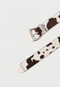 Pasek do zegarka z miękkiej skóry bydlęcej z wzorem brązowo-białych plam, z klamrą z srebrnego metalu i polerowanymi elementami metalowymi.