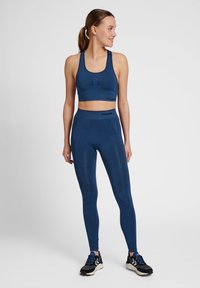 Mörkblå sport-bh och högmidjade leggings i elastiskt tyg, med texturerade detaljer och logotyp, kombinerat med svarta träningsskor.