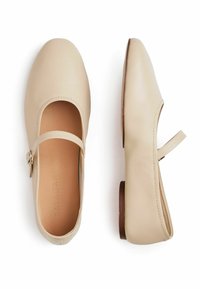 Zapatos Mary Jane de cuero color beige claro con punta redondeada, correa con hebilla y un tacón bajo marrón. Textura suave, detalles de costura mínimos.