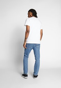 Weißes Baumwoll-T-Shirt mit kurzen Ärmeln, kombiniert mit hellblauen Jeans und schwarzen Sneakern, zeigt eine entspannte Passform und ein schlichtes Design.