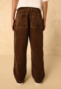 Braune Cord-Jeans mit weitem Bein und gerippter Textur, ausgestattet mit zwei Gesäßtaschen und einem elastischen Bund, der in weißen Bündchen endet.