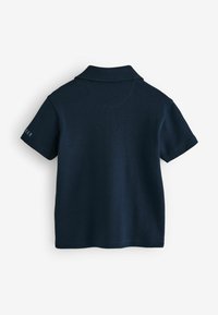 Marinblå polo skjorta i mjuk bomull, med klassisk krage, korta ärmar och broderad text på vänster ärm.