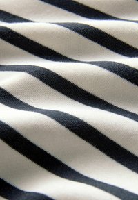 Katoenen stof met diagonale zwart-witte strepen, die een zachte textuur toont met subtiele plooien en schaduwen over het hele oppervlak.