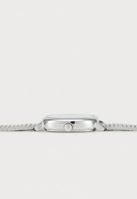 Montre argentée avec un cadran rectangulaire, boîtier en métal lisse et bracelet en maille argentée texturée. Présente une couronne proéminente sur le côté.