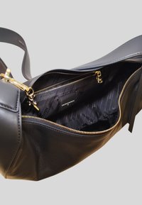 Sac en cuir noir avec une fermeture éclair dorée, doté d'une doublure intérieure texturée et d'une étiquette, mettant en avant un design spacieux et déstructuré.