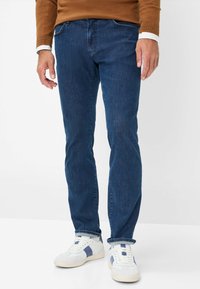 Jeans in denim blu scuro con vestibilità dritta, caratterizzati da un classico design a cinque tasche, abbinati a sneaker bianche e blu navy.