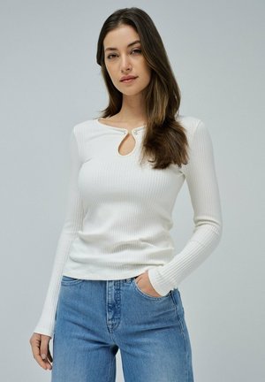 Top blanco de manga larga con canalé, que presenta un escote redondo con un corte en forma de lágrima y un cierre de botón, combinado con unos vaqueros de color azul claro.