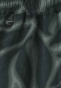 Dark gray fabric with black abstract wave patterns and visible stitching near an elastic waistband with a round metallic tag labeled Street One.