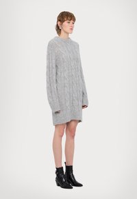 Rochie tricotată gri, cu un model în cablu, guler ribant și mâneci lungi, având o textură moale și o tiv brut.
