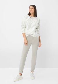 Hellgrauer Strickpullover mit dezentem Muster, kombiniert mit hellgrauen Chinos und weißen Sneakers. Das Outfit hat umgeschlagene Ärmel und einen lässigen Schnitt.