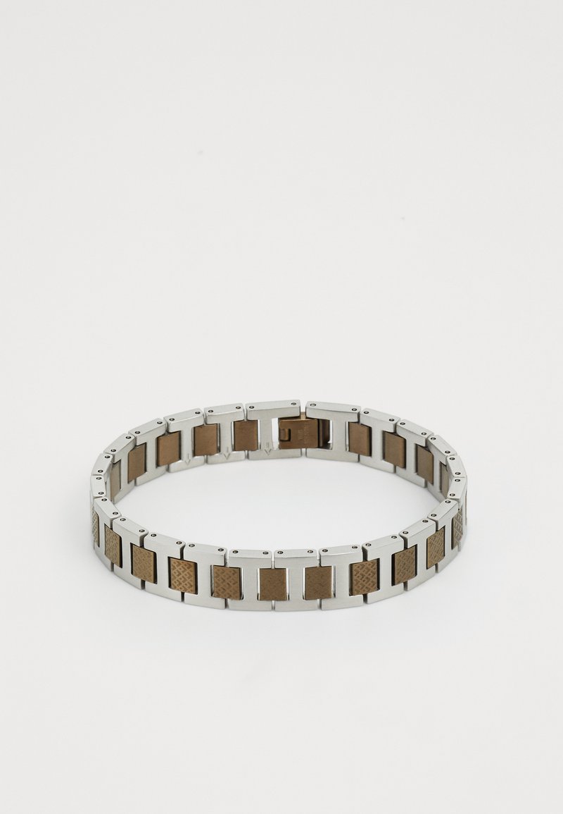 Sidabro spalvos metalo apyrankė su stačiakampiais saitais, kurie keičiasi tarp lygių ir tekstūruotų rudos spalvos akcentų. Blizgus paviršius, lanksti konstrukcija.